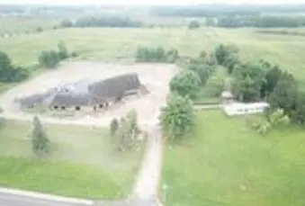 Aerial view of a large farm building surrounded by fields and trees, with a road nearby.