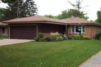 Single-story brown house with a garage and a front yard with flowers.