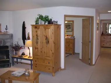 A well-lit living room featuring a wooden armoire, coffee table, and a lamp, with open doors leading to other rooms.