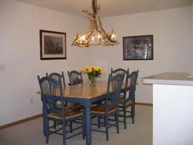 Dining room with a blue wooden table and chairs, antler chandelier above, and framed pictures on the walls.