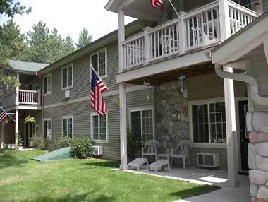 Two-story residential building with a stone façade, adorned with an american flag, featuring balconies and white rocking chairs.