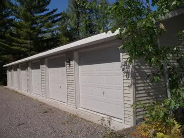 A row of beige garage doors on a single-story building, surrounded by trees under a clear sky.