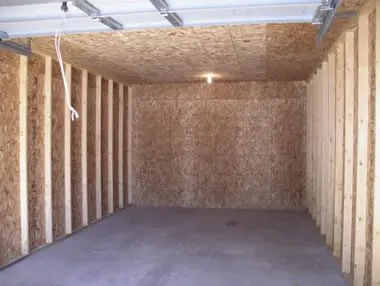 Interior of an empty shed with wooden walls and a concrete floor, illuminated by a single light.