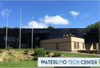 Exterior view of the waterloo tech center with its name on a sign in front, under a clear sky.