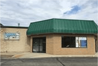 Small corner building with a green roof, housing a chiropractic clinic, on a clear day.