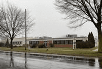 A school building on a rainy day, with wet roads and bare trees in the foreground.