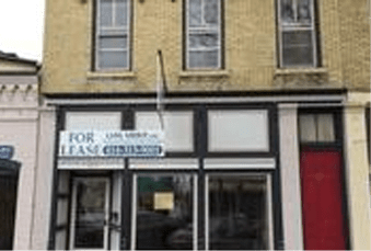 Yellow commercial building with a "for lease" sign displayed above the storefront.